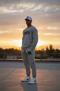 Person wearing a gray sweatshirt and pants with a cap, standing on a rooftop at sunset.